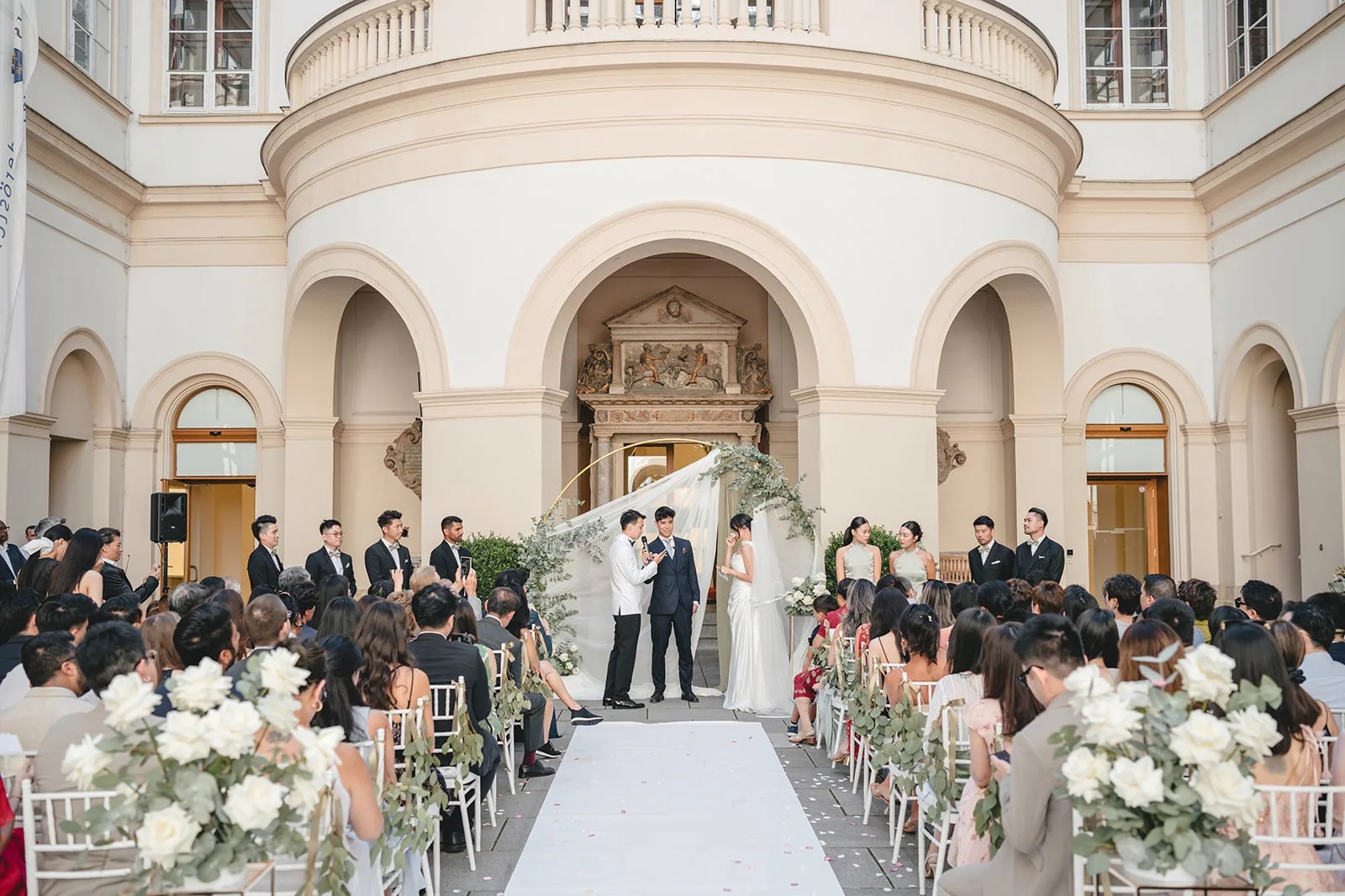 Jiamin and Anthony during their ceremony at Palais Niederösterreich, surrounded by white floral arrangements and soft daylight