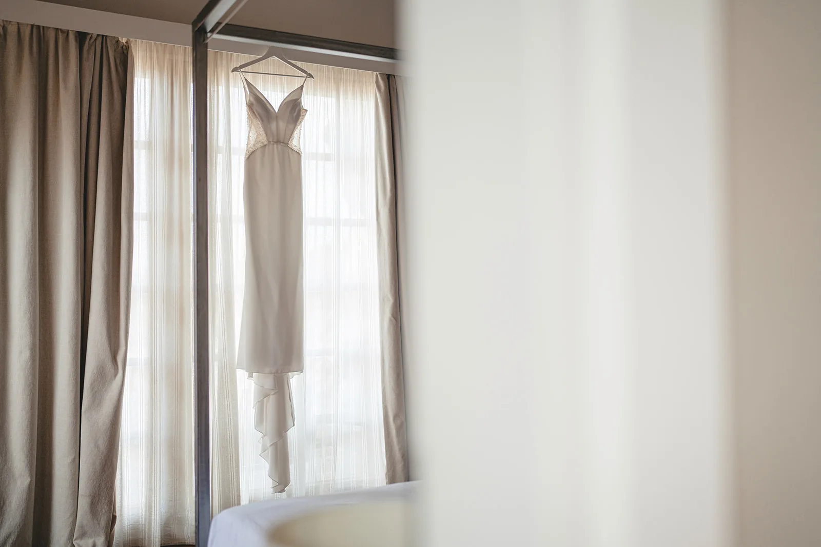 The wedding dress hanging in the hotel room window