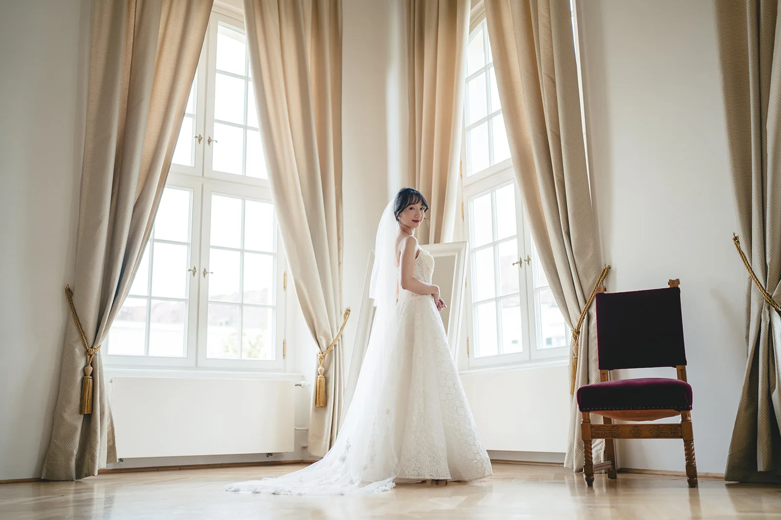 Braut im Brautkleid am hohen Fenster im Schloss Laxenburg, Niederösterreich — Hochzeitsfotografie in Europa